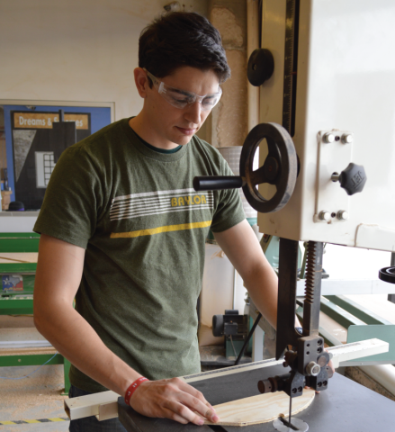 Baylor student cutting wood on a band saw at Maker's Edge