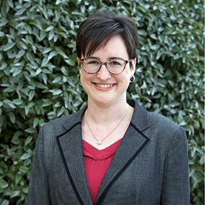Carolyn, a woman with light skin, a dark pixie cut, and glasses. She wears a bright pink top under a trim gray blazer.